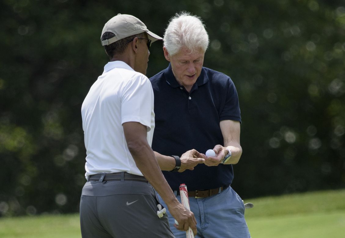 Obama hands Clinton a golf ball after putting.