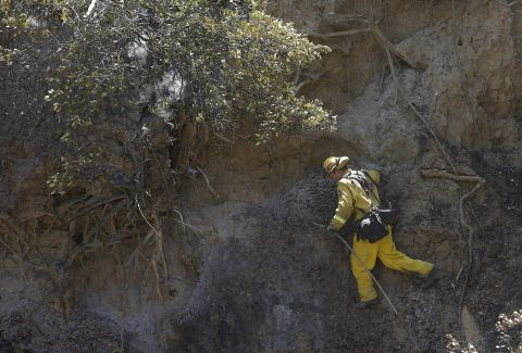 A firefighter climbs on the side of a hill while putting out hot spots in Livermore on August 20.