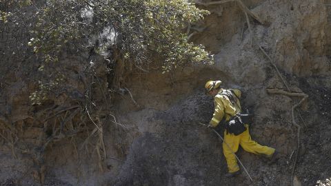 A firefighter climbs on the side of a hill while putting out hot spots in Livermore on August 20.