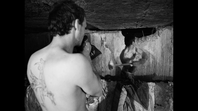 A member of the underground community demolishes a wall with a sledgehammer.