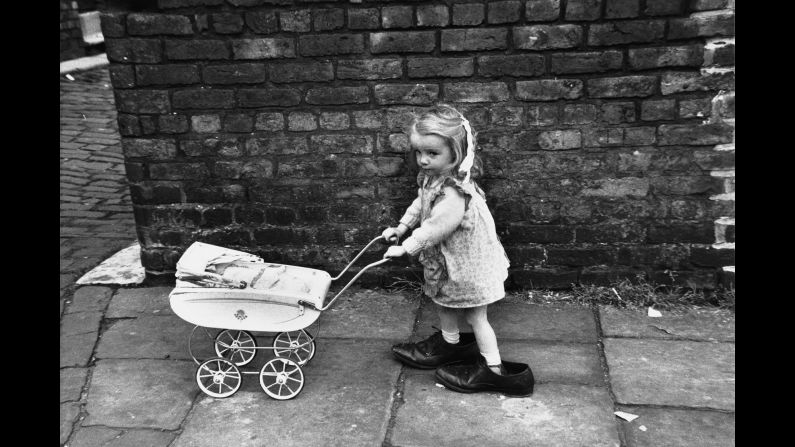 Baker was born in Salford, in greater Manchester, in 1932. After several years as a photographer for businesses and newspapers, some in London, she came back to Manchester in 1960. She couldn't help but be sympathetic with the people who were caught in the slum clearance, <a href="index.php?page=&url=http%3A%2F%2Fwww.theguardian.com%2Fartanddesign%2F2012%2Ffeb%2F01%2Fphotographer-shirley-baker-best-shot" target="_blank" target="_blank">she told The Guardian in 2012</a>: "I would go out on to the streets capturing this upheaval, photographing people I came across. ... It became an obsession." This little girl in the big shoes was photographed in Manchester in 1966.