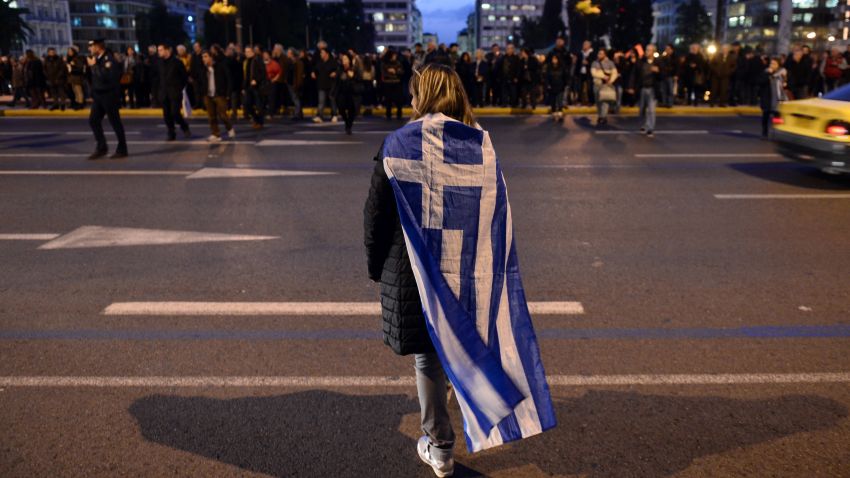 A woman wrapped in a greek flag makes her way in front of the Greek parliament  in Athens on February 5, 2015 as people gather in support of the new anti-austerity government's efforts to renegotiate Greece's international loans. About 5,000 people gathered in Syntagma Square, police said, in front of the Greek parliament, the site of violent protests at the height of the Greek crisis in 2012. Many praised the government for "defending the interests" of the Greek people. AFP PHOTO/ Louisa Gouliamaki        (Photo credit should read LOUISA GOULIAMAKI/AFP/Getty Images)