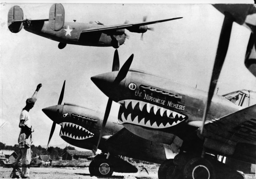 An American soldier waves good luck to a U.S. Army Air Force Liberator bomber as it crosses the shark-nosed bows of U.S. P-40 fighter planes at an advanced U.S. base in China.