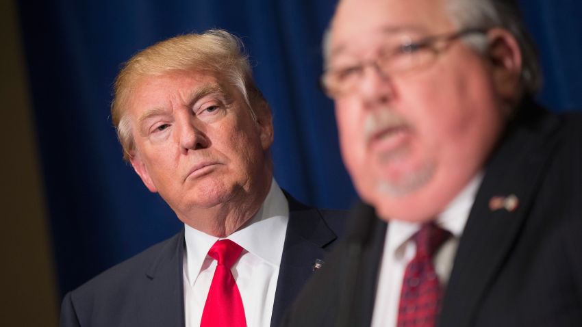 Republican presidential candidate Donald Trump listens as Sam Clovis speaks at a press conference at the Grand River Center on August 25, 2015 in Dubuque, Iowa. Clovis recently quit his position as Iowa campaign chairman for Rick Perry.