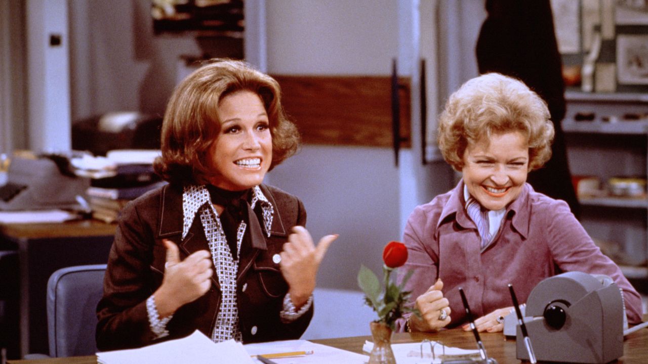 Mary Tyler Moore (as Mary Richards) (left) gives a "thumbs up" sign as she sits at her desk with Betty White (as Sue Ann Nivens) in a scene from "The Mary Tyler Moore Show" in 1975. Nivens, the "Happy Homemaker," could make a wicked Veal Prince Orloff and also cut rivals down to size.