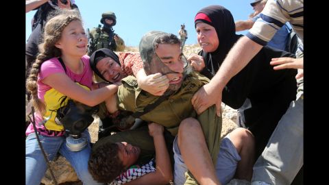 Women and children pull on the soldier's back, trying to free the boy.