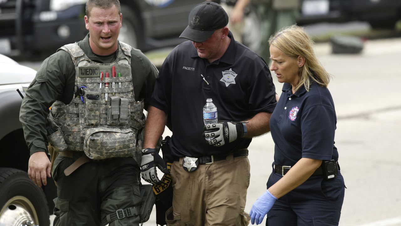 A police officer is led to an ambulance in the scorching heat.
