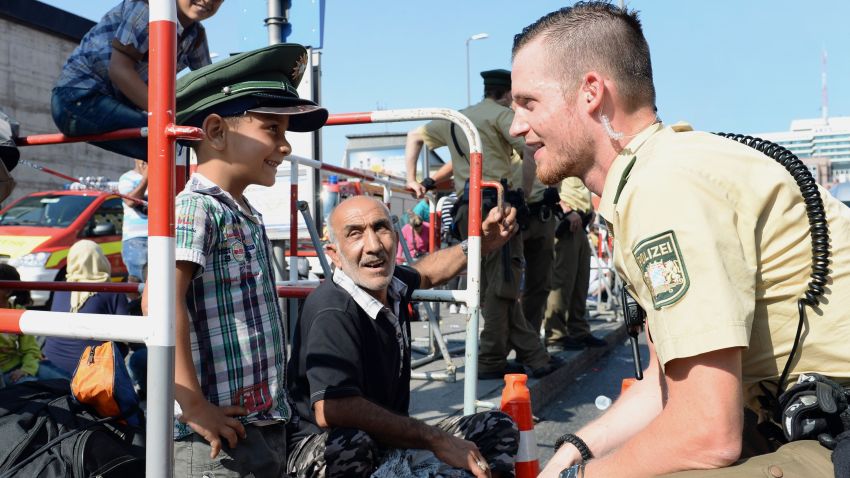 German police officer and a migrant boy joke with the officer's cap while migrants wait for a bus after their arrival at the main train station in Munich, southern Germany, September 1, 2015. Hundreds of migrants arrived in Germany during the night and the morning of September 1, 2015, with train's from Hungary and Austria. AFP PHOTO / CHRISTOF STACHECHRISTOF STACHE/AFP/Getty Images