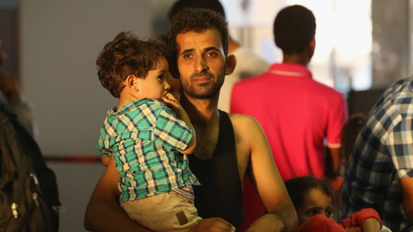 MUNICH, GERMANY - AUGUST 29:  A migrant from Syria holds one of his children in a holding area after arriving at Munich Hauptbahnhof main railway station and being detained by police on August 29, 2015 in Munich, Germany. According to police hundreds of migrants are arriving in southern Germany daily, either via people smugglers from Hungary along the A3 highway or via trains coming from Italy. Germany is expecting to receive 800,000 asylum-seeking migrants this year and is struggling to cope with the record number.  (Photo by Sean Gallup/Getty Images)