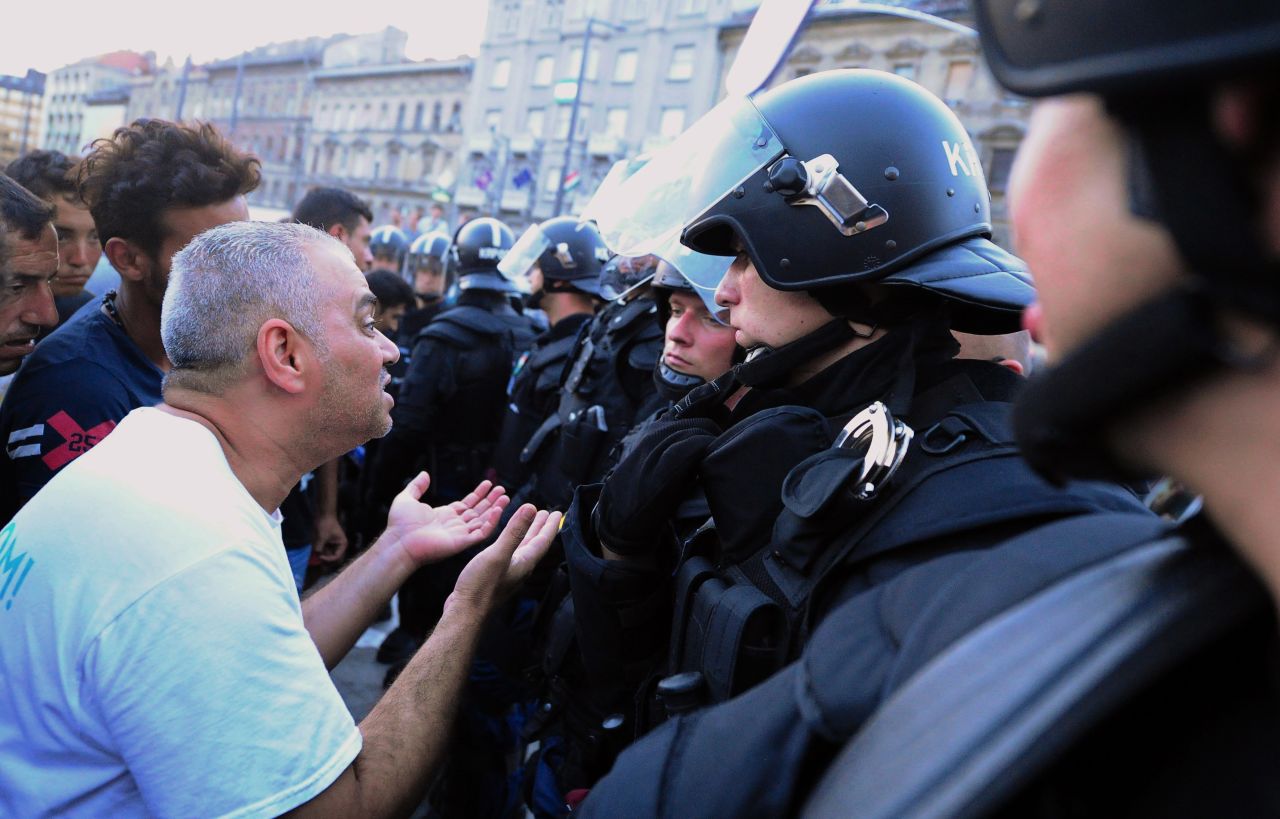 Refugees and migrants speak with riot police officers in front of Keleti station.