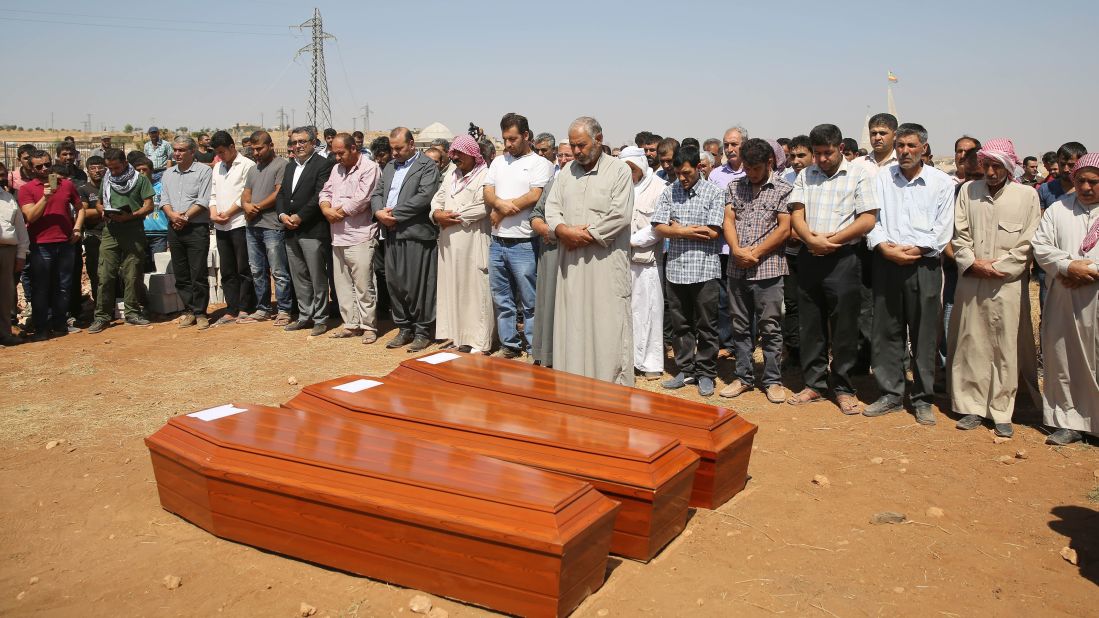 People stand near the coffins during the burial ceremony in Kobani on September 4, 2015.