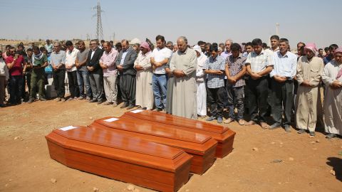 People stand near the coffins during the burial ceremony in Kobani on September 4, 2015.