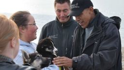 US President Barack Obama reaches out to pick up a puppy belonging to musher John Baker (2nd R) in Kotzebue, Alaska on September 2, 2015.