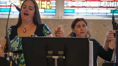 Danielle Quaglia (left), a 30-year-old who's attended Saint Charles Borromeo her whole life, sings the Lord's Prayer with a Spanish choir group she's just joined. "I love to sing...to share my talent that God gave me, hopefully to inspire others and make others feel welcome," she says.