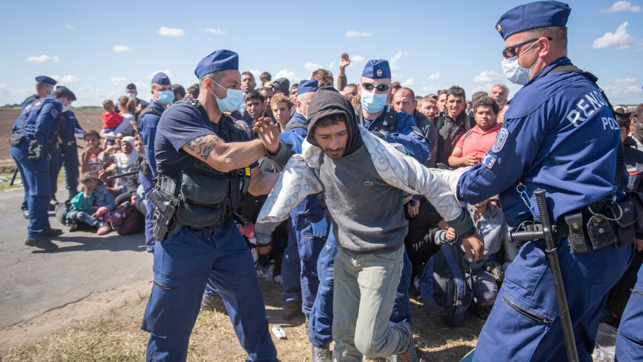 ROSZKE, HUNGARY - SEPTEMBER 07:  Migrants who have just crossed into Hungary are kept under control by the police as they wait for buses to take them to a reception camp on September 7, 2015 in Roszke, Hungary. As the migrant crisis in Europe continues and estimated 18000 people arrived in Germany over the weekend thousands more following in their wake along the Balkan route.  (Photo by Matt Cardy/Getty Images)