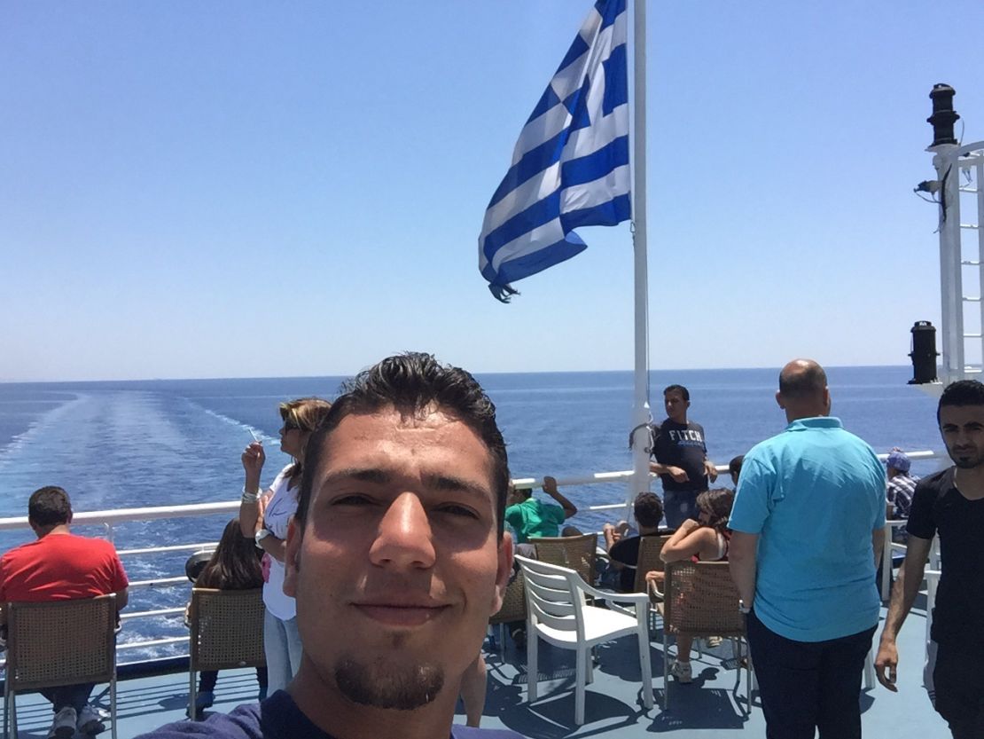 Modamani takes a selfie on board a boat with a Greek flag waving in the background. 