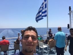 Modamani takes a selfie on board a boat with a Greek flag waving in the background.