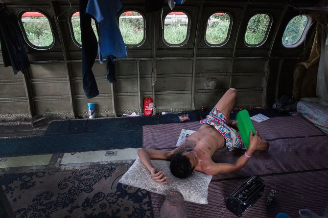 A Thai man fans himself with a piece of plastic while listening to a battery-powered radio in his home in one of the disused airplanes.  