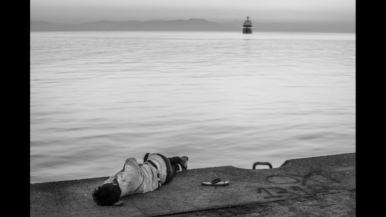 A migrant sleeps at the port of Kos. In the background is Turkey's coast.