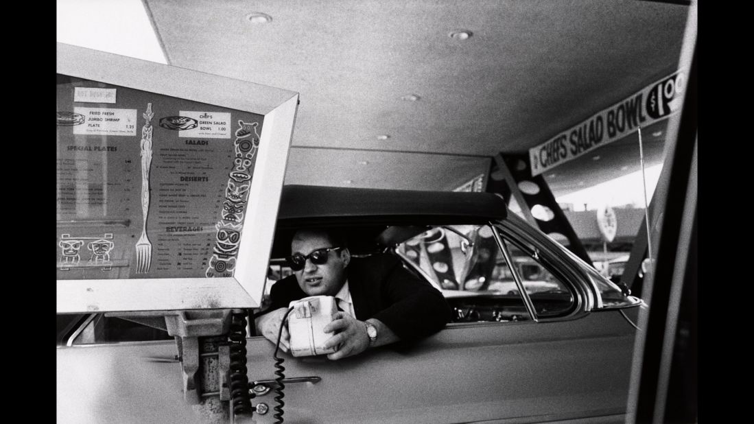 A man uses a microphone to order food from a drive-in diner. This photo was also used as the cover of the Beastie Boys album "Ill Communication."