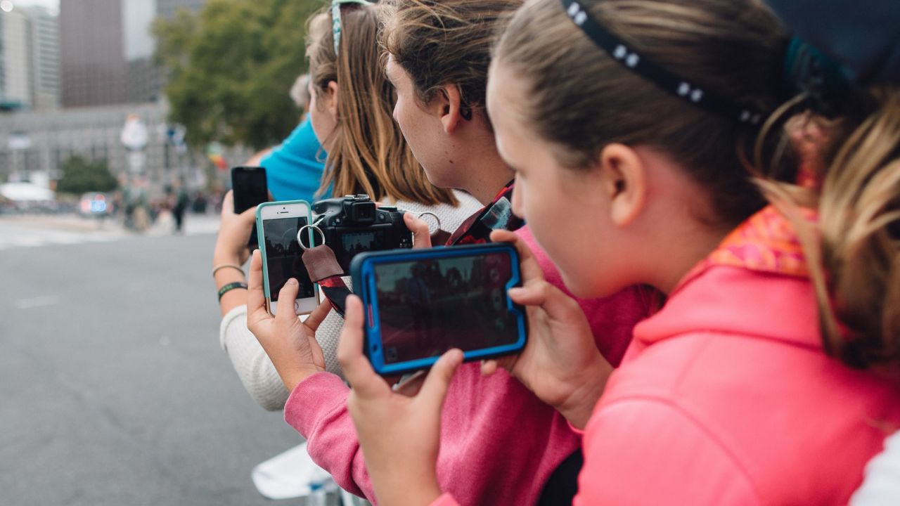 People eagerly prepare their phones to capture imagery as they wait for the Pope to pass by.