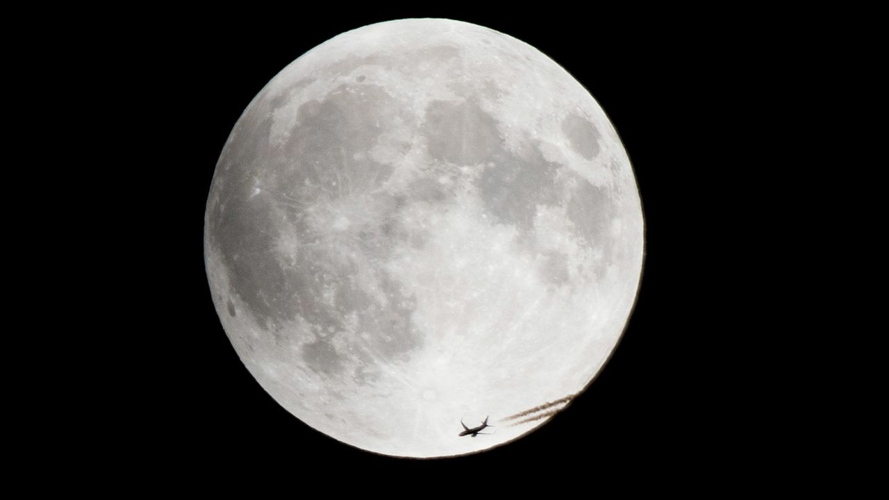 A plane passes by the rising supermoon in Montreal.