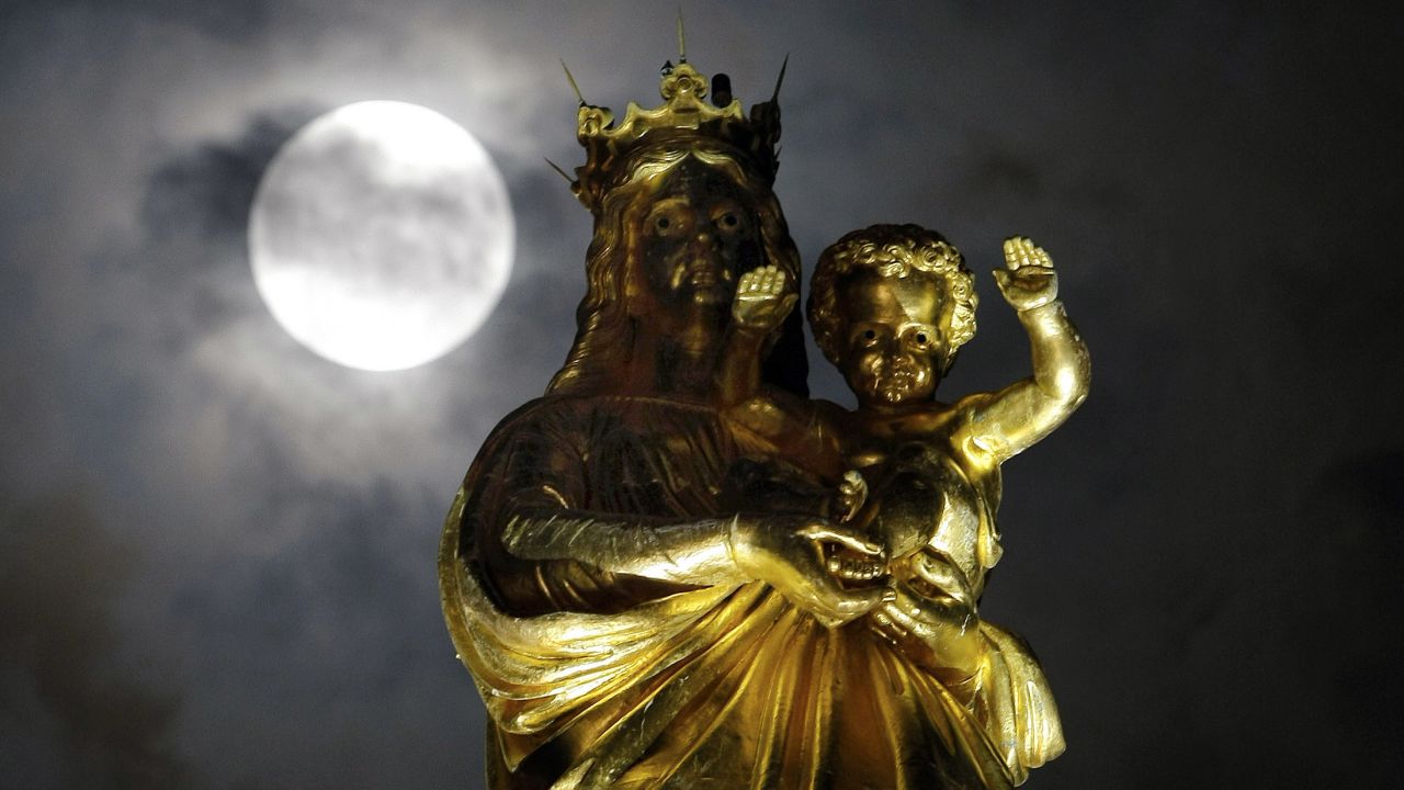 The supermoon passes by a statue of the Virgin Mary and the Child at Notre Dame de La Garde basilica in Marseille, France.