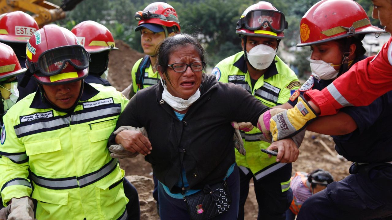 Rescue workers help a woman after she identified two family members at the site of the landslide on Saturday, October 3.