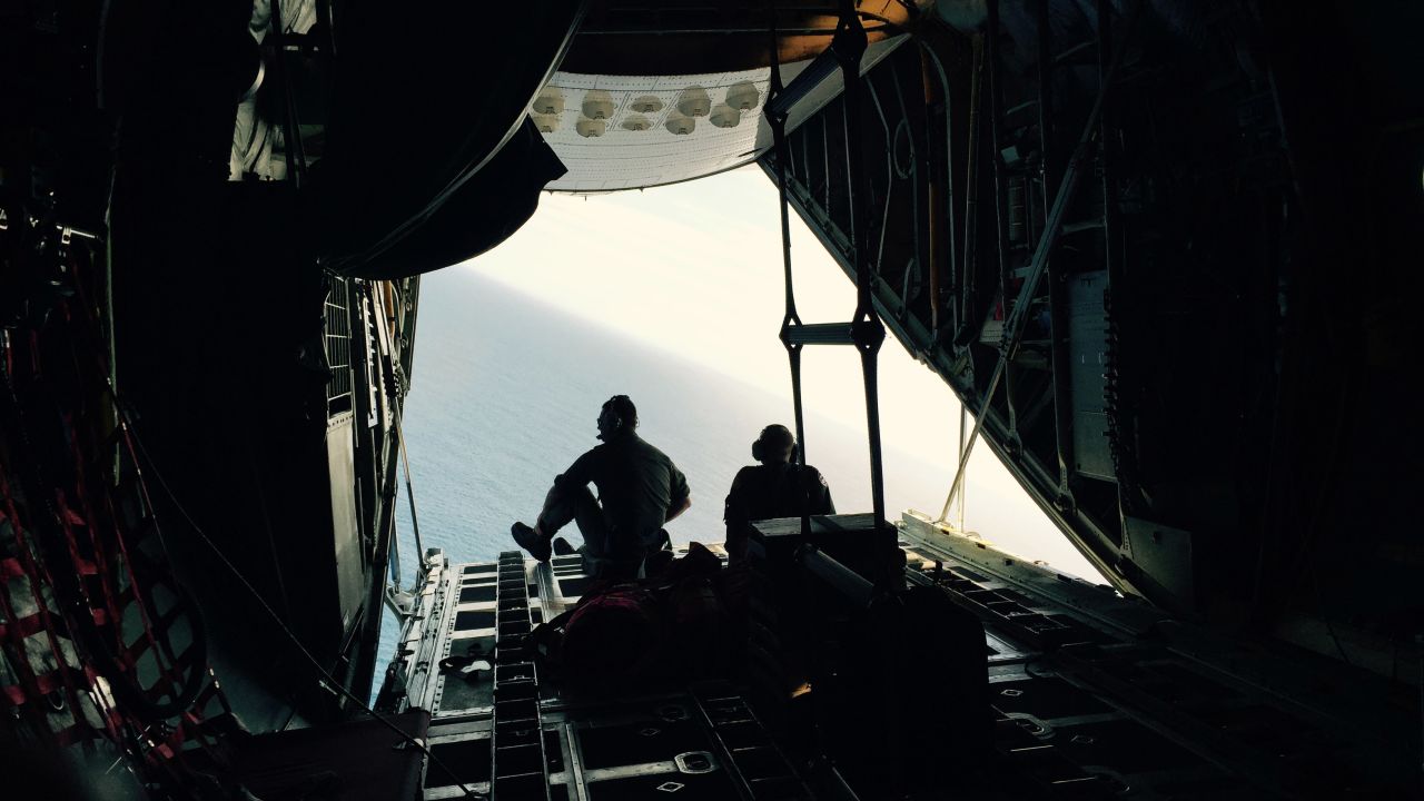 The plane makes a sharp bank to "orbit," or fly back over, a piece of debris that the crew wants to check. On the second pass, the cockpit crew gives it another look, as will the crewmember operating the onboard camera. Here, Petty Officers 3rd Class Chris LaBelle, left, and Mark Strock sit on the edge of the cargo door in hopes of getting a better perspective on the debris.