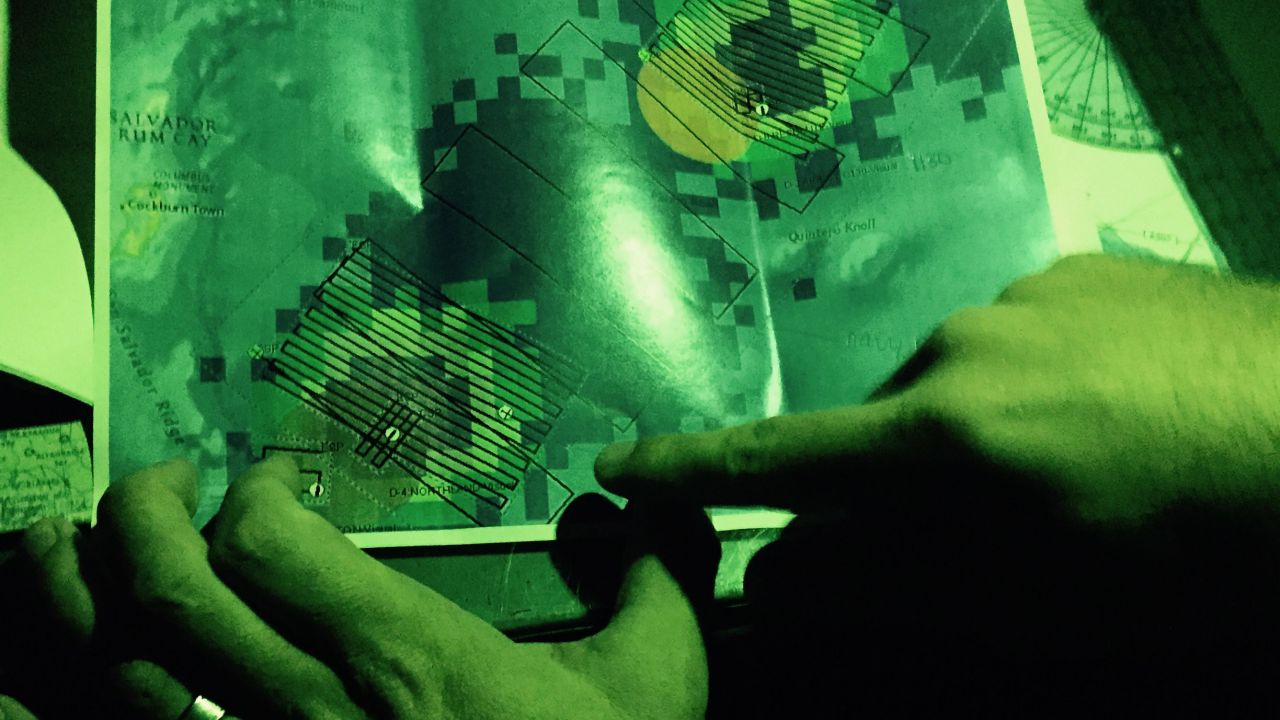 LaBelle, the navigator, points out the plane's planned grid en route to the search area. The land mass to the left is San Salvador Island, Bahamas, and the grid requires that pilots fly in a 44-mile lane in one direction, make a U-turn almost two miles wide, and then fly back 44 miles parallel to the previous lane. The total flight was about 700 miles, roughly the distance from Minneapolis to Denver.