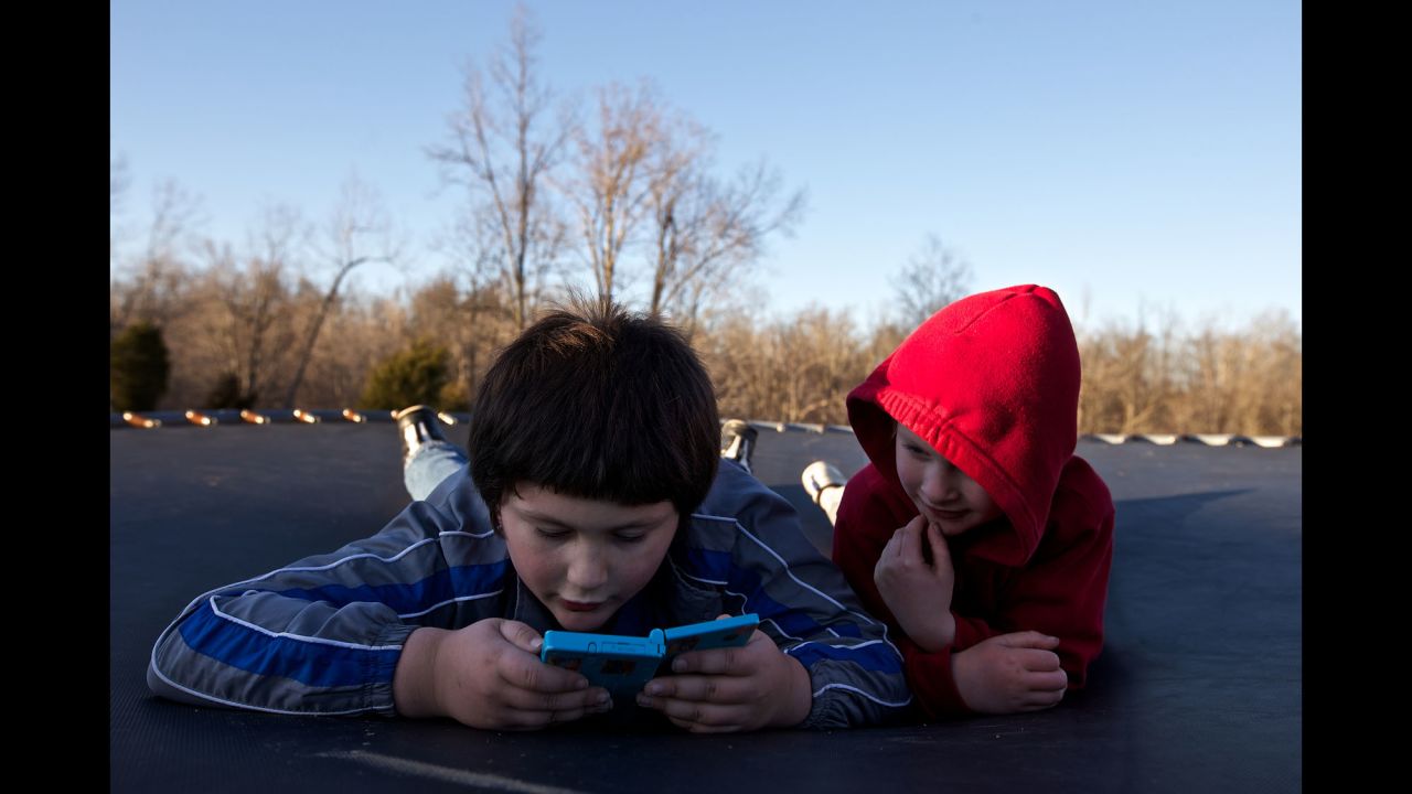 Skylor and Faron Jr. play a video game while resting on a trampoline at their home.