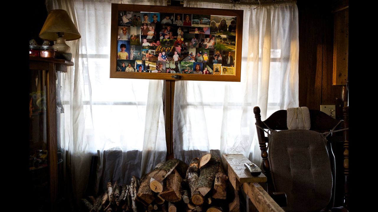 A frame with an array of family photos hangs over a freshly cut stack of firewood at the family's home.