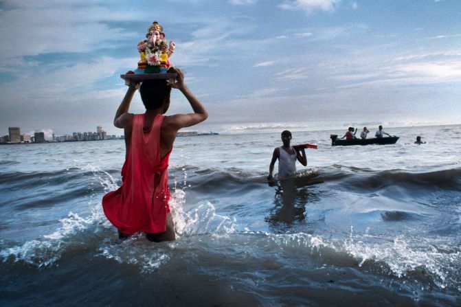 This image depicts a devotee carrying a statue of Lord Ganesh into the waters of the Arabian Sea, during the immersion ritual off Chowpatty Beach in Mumbai, 1993<br /><br />"For all the silliness and vulgarity that McCurry photographs in modern urban India, he never forgets that India is still a profoundly sacred land," says Dalrymple.<br /><br />"It is, after all, a country with 2.5 million places of worship, but only 1.5 million schools and barely 75,000 hospitals. Pilgrimages account for more than half of all package tours, and the bigger pilgrimage sites vie with the Taj Mahal in popularity: 17.25 million trekked to the shrine of Vaishno Devi."