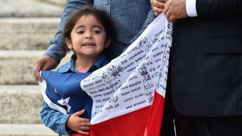 A little girl waiting for Pope Francis holds a Chilean national flag with the names of rescued miners. The men gave the Pope a signed helmet and an enlarged framed message.