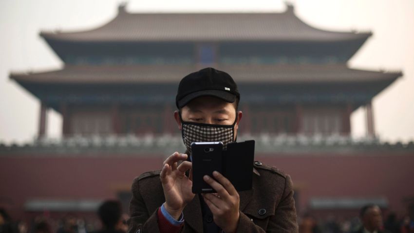BEIJING, CHINA - NOVEMBER 20:  A Chinese man wears a mask to protect against pollution as he uses his smartphone on a hazy day outside the Forbidden City November 20, 2014 in Beijing, China. United States President Barack Obama and China's president Xi Jinping agreed on a plan to limit carbon emissions by their countries which are the world's two biggest polluters at a summit in Beijing last week.  (Photo by Kevin Frayer/Getty Images)