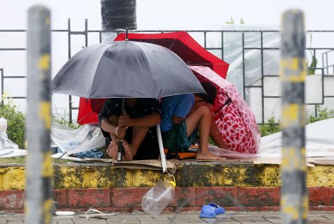 Residents huddle under umbrellas as strong winds and slight rain are brought by Typhoon Koppu on October 18 in Manila. 