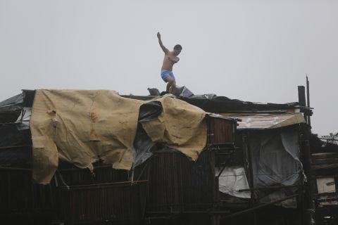 A man is thrown off balance by strong winds while he tries to reinforce the roof of his house on October 18 in Navotas.