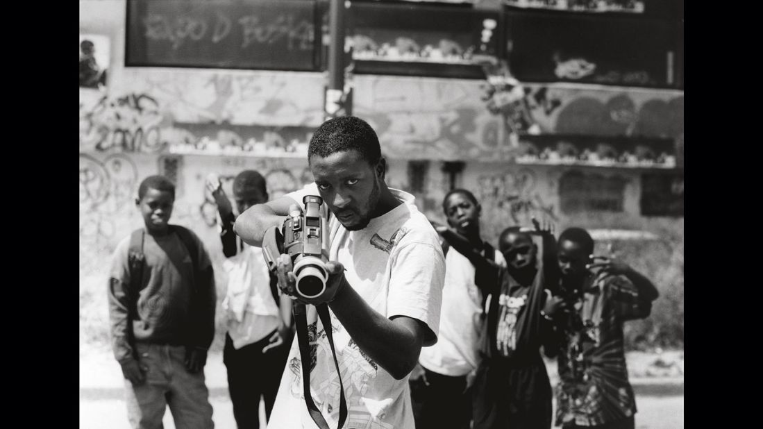 JR took this photo of young French-Malian man Ladj Ly's as part of his "Portrait of a Generation" project. At first glance the man looks as though he's pointing a gun, but it is in fact a camera -- the photo challenges the ideas of clichés in visual culture. <br />