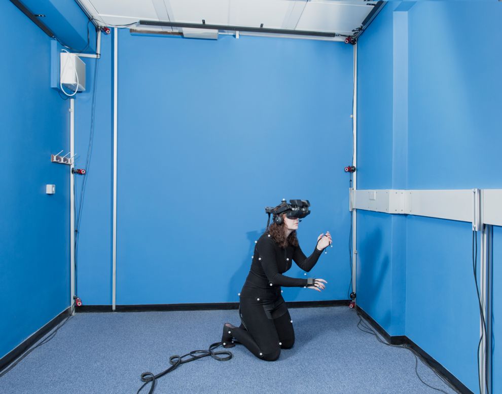 Psychologist/neuroscientist Dr. Caroline Falconer of the University of Nottingham is developing ways to use virtual reality to treat depression. In the photo, Falconer demonstrates a head-mounted, high-definition, 3-D display with full-body tracking. Patients use this gear to spatially substitute their own bodies with an avatar. Falconer is shown reaching out to comfort a crying, virtual child in a computer program aimed at cultivating self-compassion.