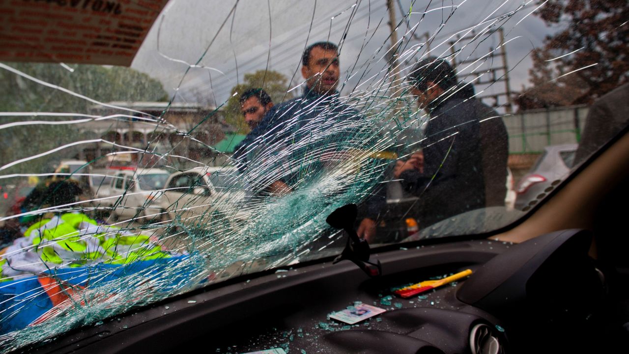 People stand next to a car damaged by a tree branch in Srinagar, India.