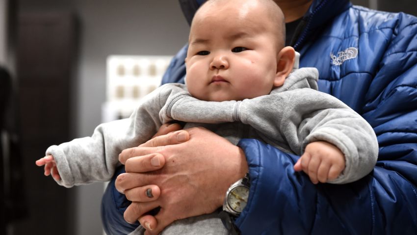 This picture taken on January 19, 2015 shows a Chinese baby in the arms of his father at a furniture store in Beijing.  China's working-age population continued to fall in 2014, the government said on January 20, as Beijing struggles to address a spiralling demographic challenge made worse by its one-child policy.    AFP PHOTO/GOH CHAI HIN        (Photo credit should read GOH CHAI HIN/AFP/Getty Images)