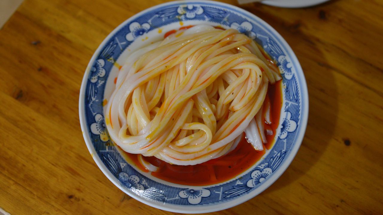 Rice noodles are cooked, cooled and thinly sliced. The noodles are often served in a sauce made of chili oil, pepper powder, vinegar and diced garlic. Then it's garnished with bean sprouts and sliced cucumber.