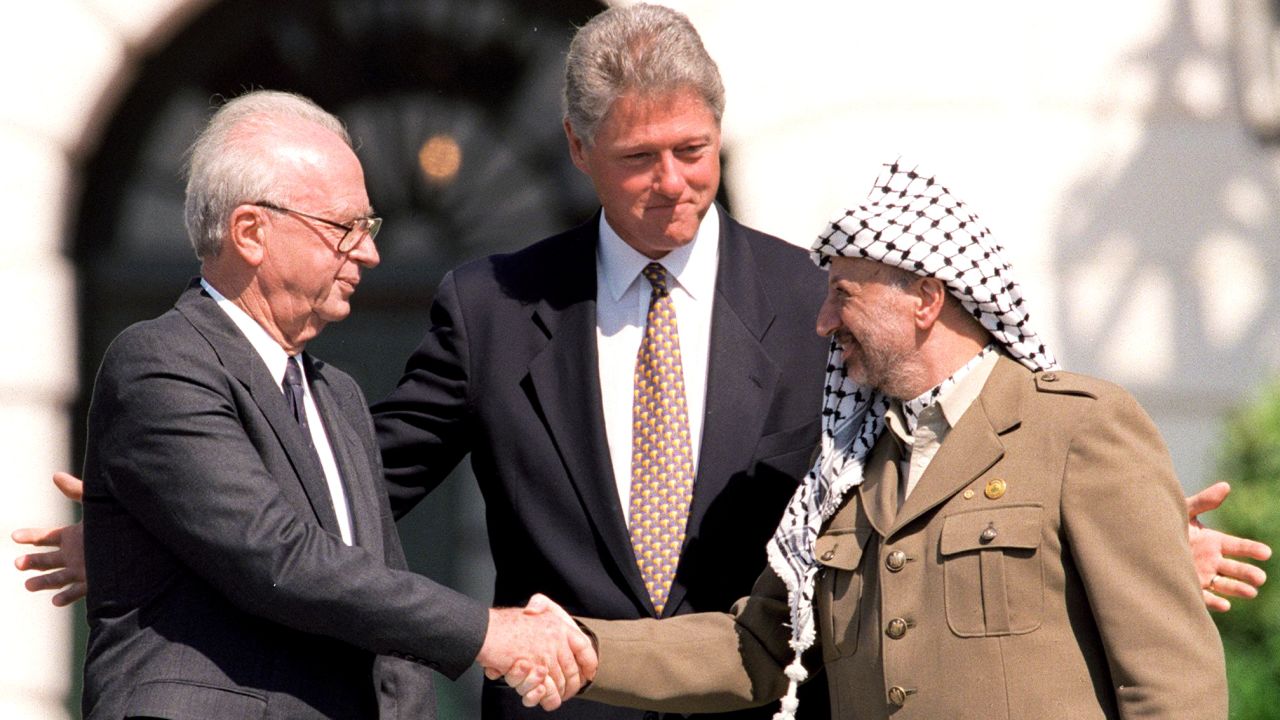 U.S. President Bill Clinton stands between Israeli Prime Minister Yitzhak Rabin, left, and PLO Chairman Yasser Arafat as they shake hands on September 13, 1993.