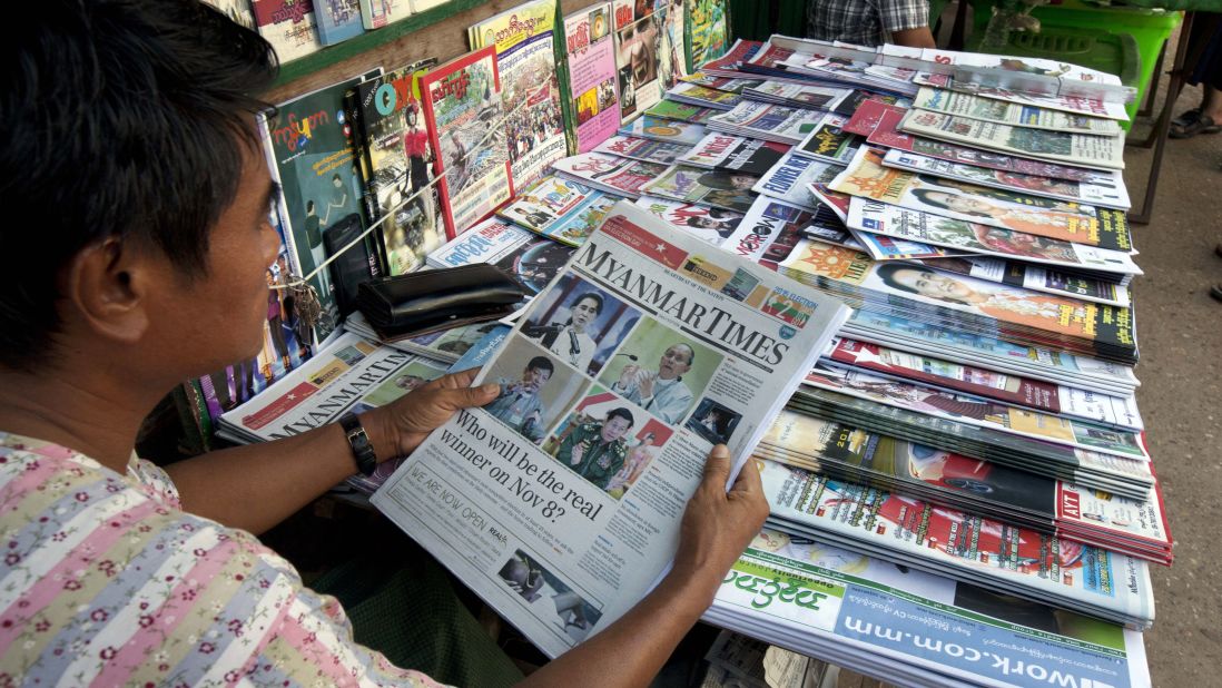A vendor reads a local weekly journal showing a portrait of Myanmar opposition leader Aung San Suu Kyi, President Thein Sein and others.
