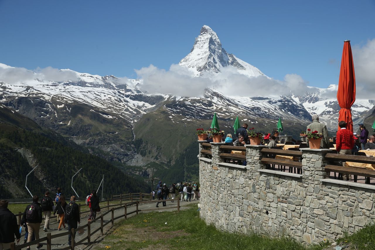 Hikers prepare for an outing as the Matterhorn looms behind the terrace of the Sunnegga Station restaurant near Zermatt, Switzerland.