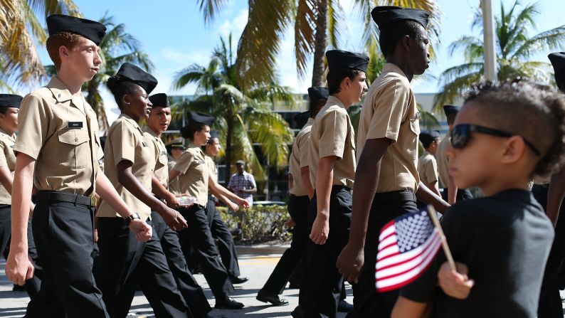 High school students in the Navy Junior ROTC program march past Xavier Barnett, front right, during a parade in Miami Beach, Florida.  