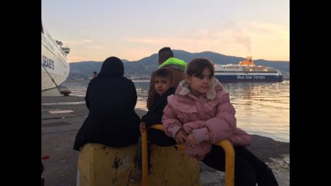Farah (R), 10, is from Baghdad. She has been waiting with her younger brother and parents for a boat to Athens for two days. When asked why they are leaving, she says, "the situation in Baghdad is not good, that's what daddy said."