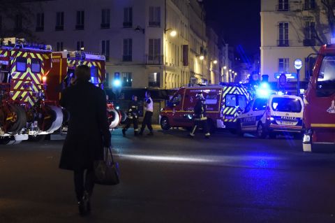 A woman walks past police and firefighters in the Oberkampf area of Paris.