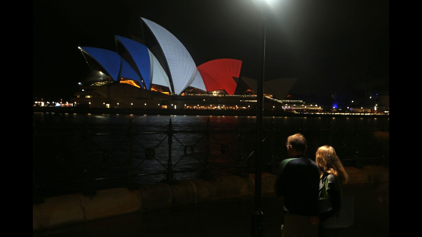 A couple surveys the signature sails of the Sydney Opera House lit in the colors of the French flag in Sydney on November 14.