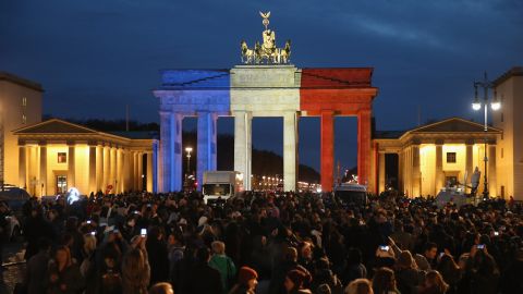 The Brandenburg Gate in Berlin, Germany stands illuminated in the colors of the French flag as people arrive to lay candles and flowers at the gate of the adjacent French Embassy.